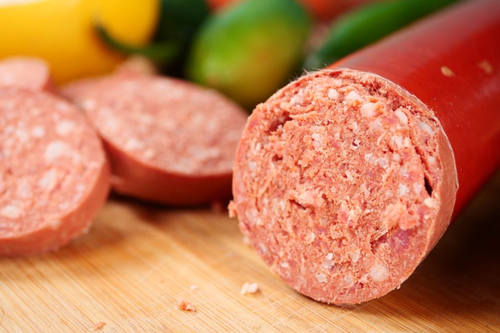 Батон сирокопченої ковбаси з нарізаними скибками на дошці